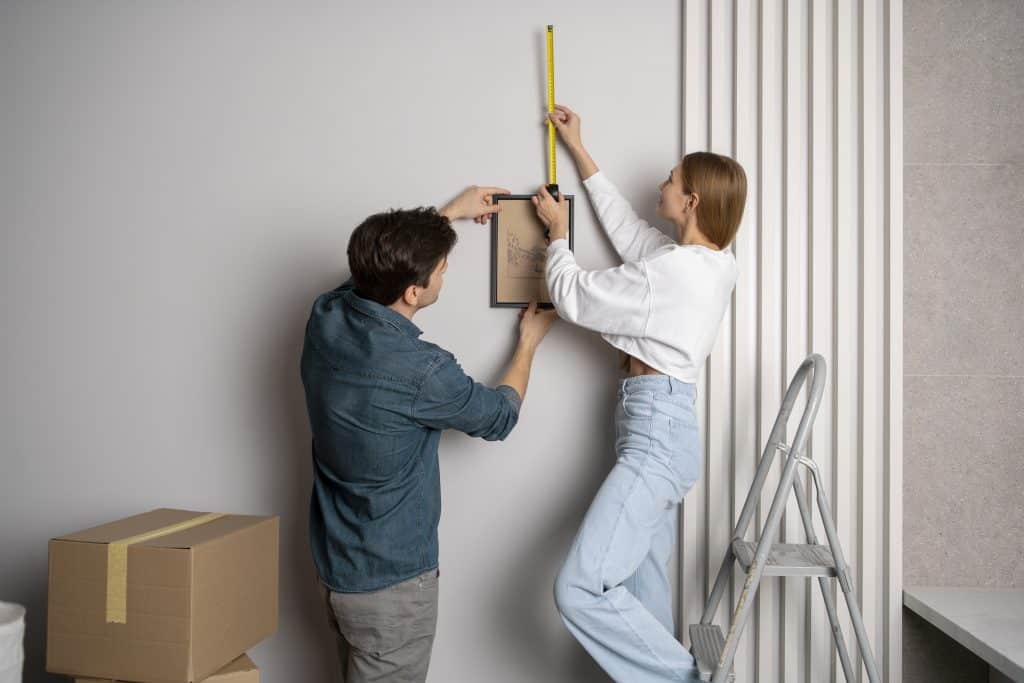 Couple mesurant un mur pour accrocher un cadre lors d’un emménagement