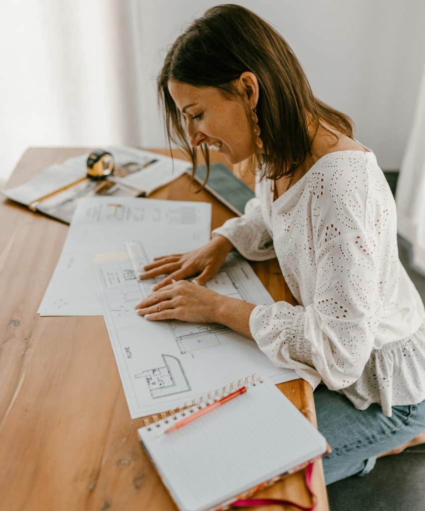 Femme assise mesurant un plan d’aménagement sur une table basse avec une règle