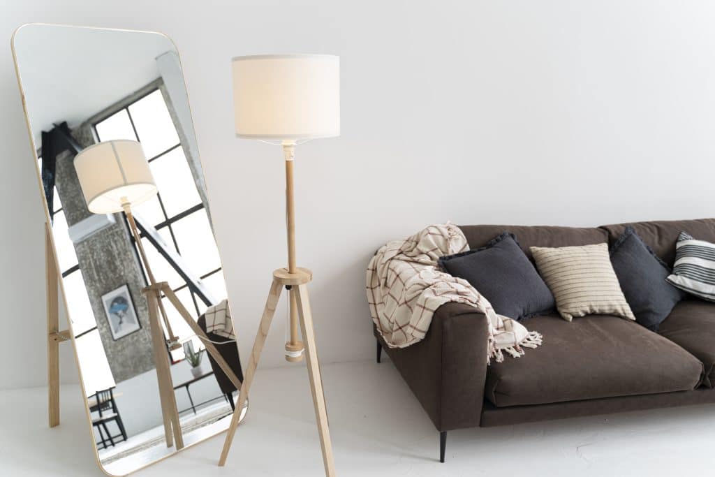Pièce avec canapé et luminaire, miroir reflétant une partie de la pièce