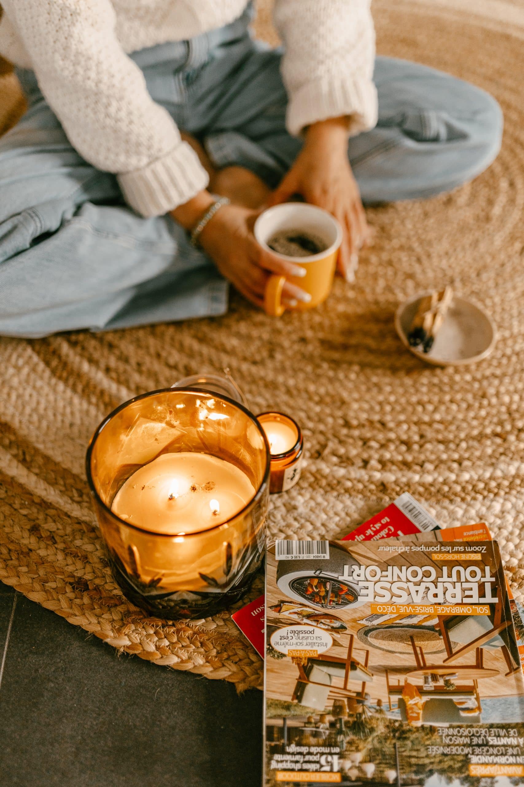 Femme assise par terre avec une tasse de café, entourée de bougies et de magazines